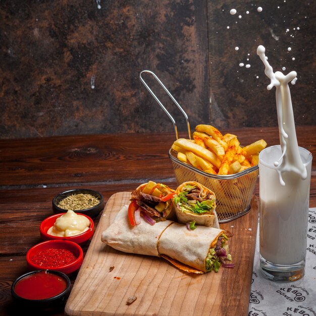 Vista lateral shawarma con papas fritas y ayran y salpicaduras en utensilios de cocina