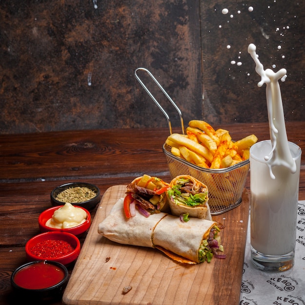 Vista lateral shawarma con papas fritas y ayran y salpicaduras en utensilios de cocina