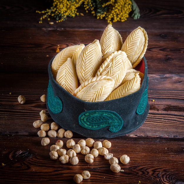 Vista lateral shekerbura con nueces y flores de mimosa en sombrero nacional en mesa de madera