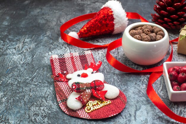 Vista lateral del sombrero de santa claus y el calcetín de año nuevo de chocolate cornel regalo de cono de conífera roja sobre superficie oscura