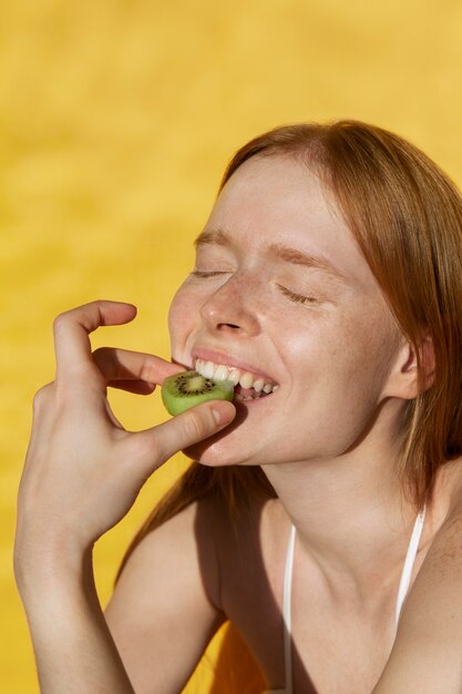 Vista lateral sonriente mujer comiendo kiwi