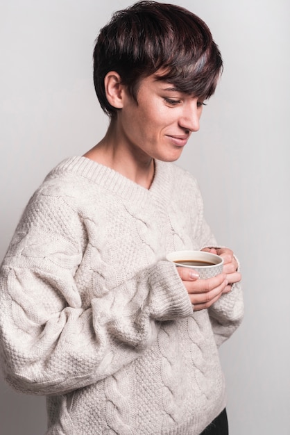 Vista lateral de la sonriente mujer enferma con taza de café sobre fondo blanco