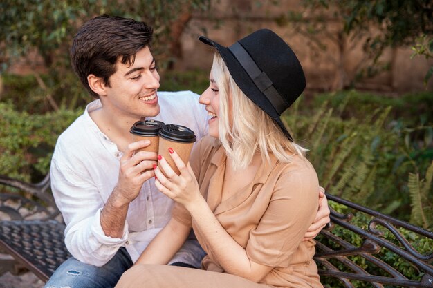 Vista lateral de la sonriente pareja en el parque con tazas de café