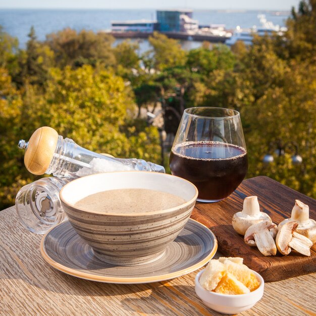 Vista lateral sopa de champiñones con champiñones, vino en una mesa de madera lighton en restaurante junto al mar