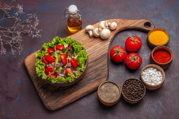 Vista lateral superior de la comida en la ensalada de tablero con tomates, pimientos verdes y aceite de lechuga y diferentes especias.