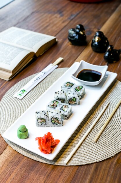 Vista lateral sushi piel maki rolls con salsa de soja jengibre y wasabi en un plato y un libro sobre la mesa