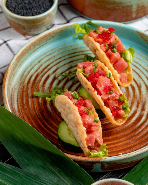 Vista lateral de tacos de salmón con caviar rojo y cebolla verde en un plato