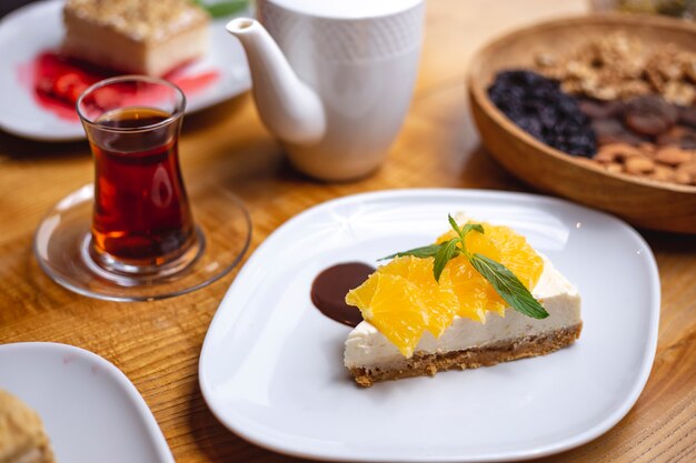 Vista lateral tarta de queso con rodajas de naranja y un vaso de té