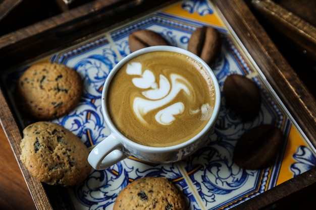 Vista lateral de la taza de capuchino con galletas de avena en una bandeja