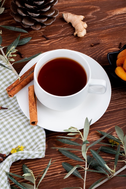 Foto gratuita vista lateral de una taza de té con albaricoques secos y palitos de canela en madera