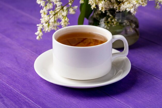 Vista lateral de la taza de té con flores sobre una superficie de color púrpura brillante