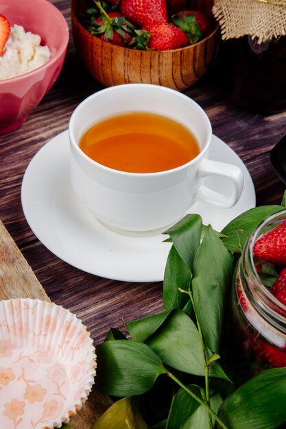 Vista lateral de una taza de té con fresas maduras frescas en rústico