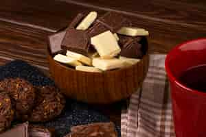 Foto gratuita vista lateral de una taza con té galletas de avena y trozos de chocolate negro y blanco en un recipiente de madera sobre fondo rústico