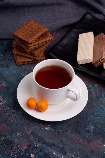 Vista lateral de una taza de té con galletas en la oscuridad