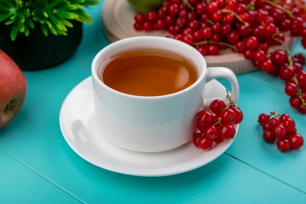 Vista lateral taza de té con grosellas rojas con manzanas sobre un fondo azul claro