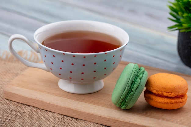 Vista lateral de la taza de té con macarons en una tabla para cortar