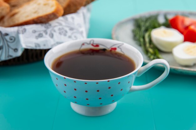 Vista lateral de la taza de té con pan y eneldo de huevo de tomate sobre fondo azul.