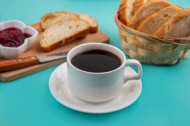 Vista lateral de la taza de té con rebanadas de pan y mermelada de frambuesa en la tabla de cortar sobre fondo azul.