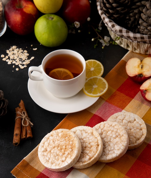 Vista lateral taza de té con rodajas de limón y canela con manzanas sobre la mesa