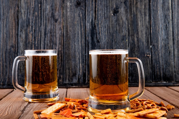 vista lateral Tazas de cerveza con chips de chuck duro y galletas en la mesa de madera