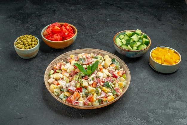 Foto gratuita vista lateral del tazón de fuente de ensalada de verduras en el centro con tazones de verduras en el lado sobre fondo gris oscuro