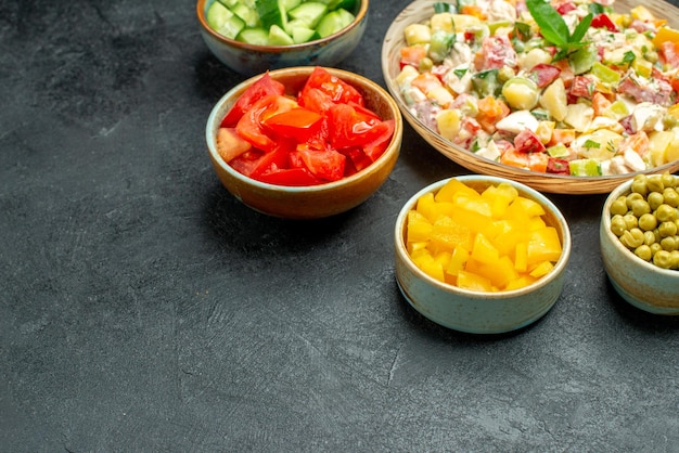 Foto gratuita vista lateral del tazón de fuente de ensalada de verduras con tazones de verduras en el lado sobre fondo verde oscuro