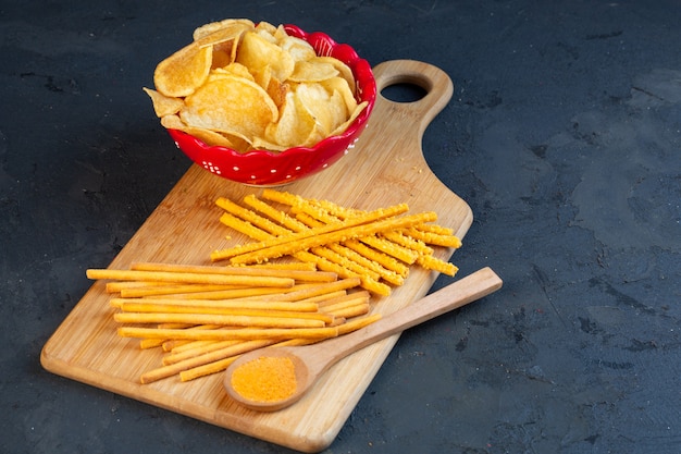 Foto gratuita vista lateral de un tazón con papas fritas y palitos de pan con sal esparcidos sobre una tabla para cortar madera en negro