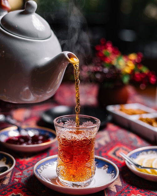 Foto gratuita vista lateral de té negro en vidrio en forma de pera sobre la mesa