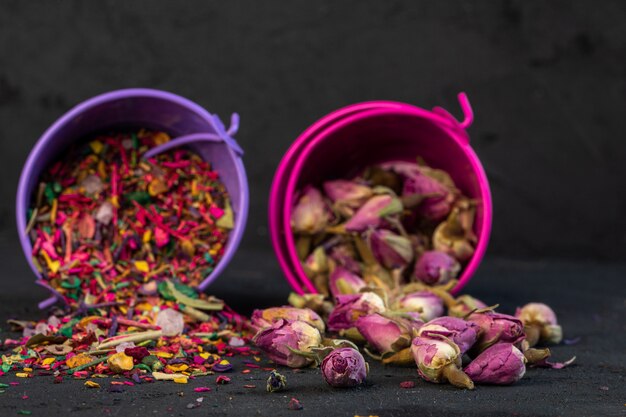 Vista lateral de té de rosas y pétalos de flores secas dispersos de pequeños cubos en negro