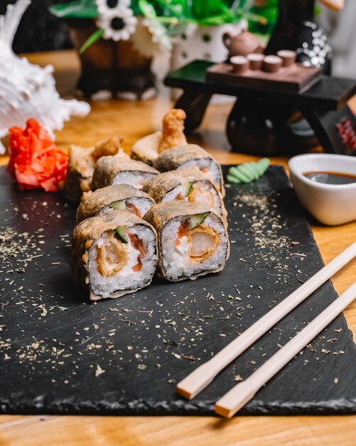 Vista lateral tempura roll de sushi con salmón, pepino, jengibre, wasabi, salsa de soja y semillas de sésamo en una bandeja