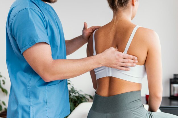 Vista lateral del terapeuta osteopático masculino comprobando el hueso de la escápula del paciente femenino