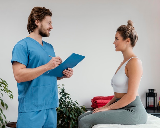 Vista lateral del terapeuta osteopático masculino con portapapeles de firma paciente femenino en la clínica