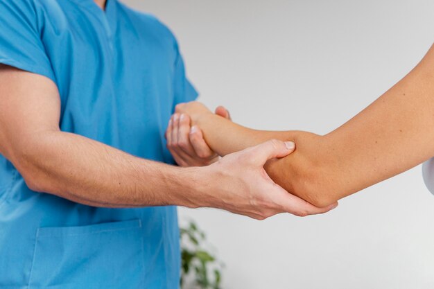 Vista lateral del terapeuta osteopático masculino que controla el movimiento de la articulación del codo del paciente femenino