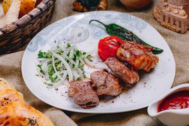 Vista lateral tikya kebab con cebolla verde salsa de tomate picante picante y pan sobre la mesa