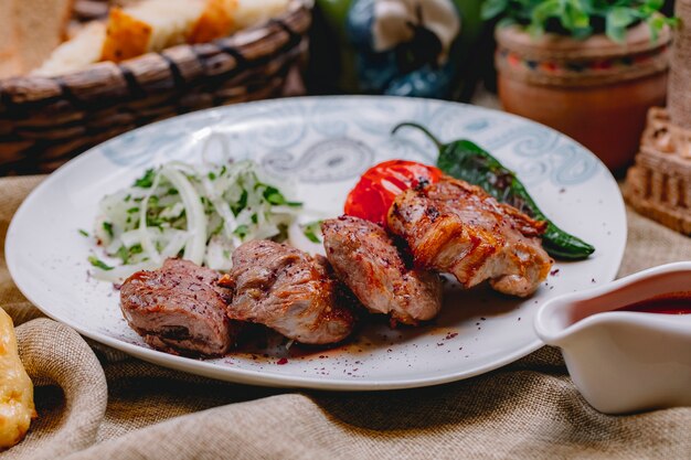 Vista lateral de tikya kebab con tomate a la parrilla, pimiento picante, cebolla y verduras en un plato