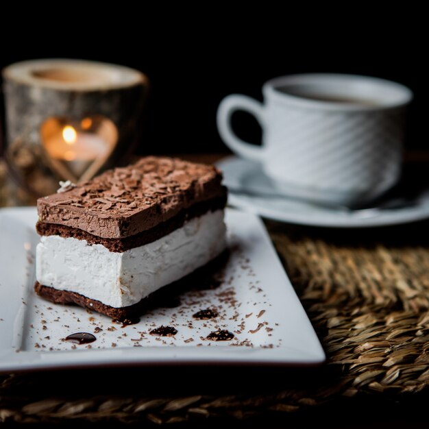 Vista lateral tiramisú de chocolate con taza de té y velas y plato blanco en servilletas