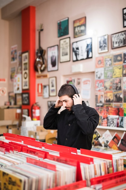 Vista lateral de tiro medio de un hombre joven escuchando música en una tienda de vinilo