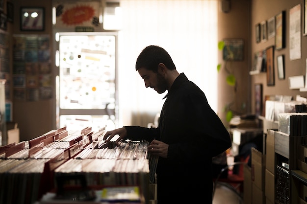 Vista lateral de tiro medio de un hombre joven que busca vinilos en la tienda.