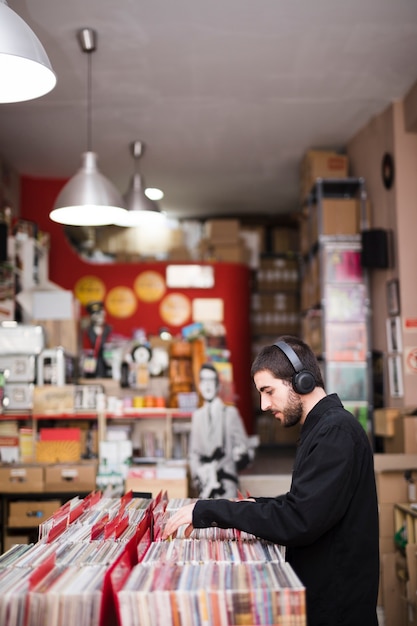 Vista lateral de tiro medio de un hombre joven que busca vinilos en la tienda.