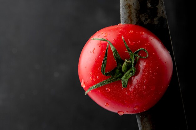 Vista lateral de tomate maduro húmedo con un cuchillo en fondo negro