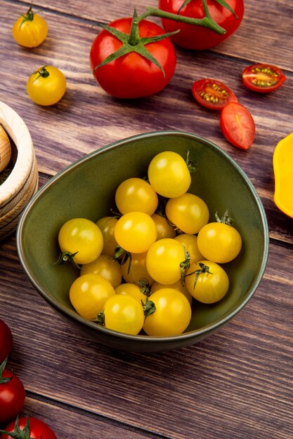 Vista lateral de tomates amarillos en un tazón con rojos sobre superficie de madera