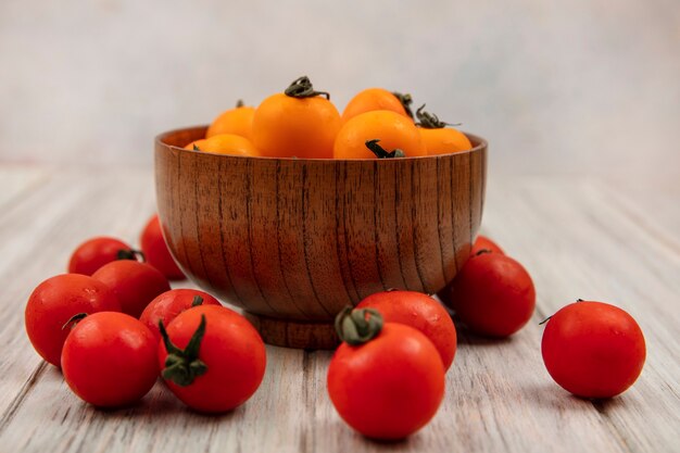 Vista lateral de tomates anaranjados suaves en un cuenco de madera con tomates rojos aislados sobre una superficie de madera gris