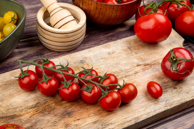 Vista lateral de tomates en tabla de cortar con otros trituradora de ajo en mesa de madera