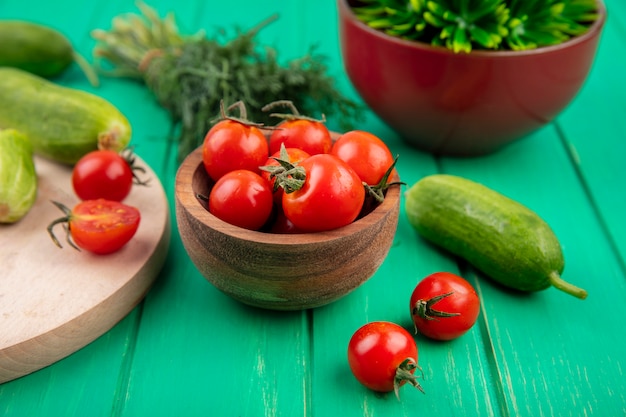 Vista lateral de tomates en un tazón y eneldo de pepino alrededor en verde