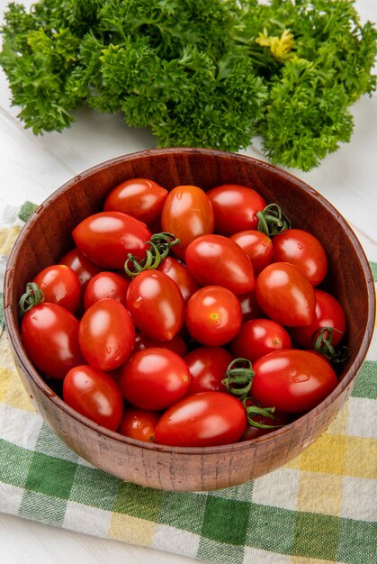 Vista lateral de tomates en un tazón sobre tela con cilantro chino en la mesa de madera