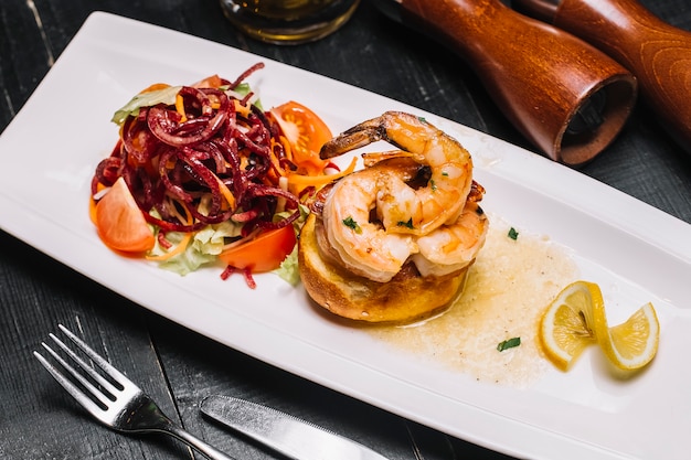 Vista lateral tostadas de camarones con ensalada de verduras y una rodaja de limón