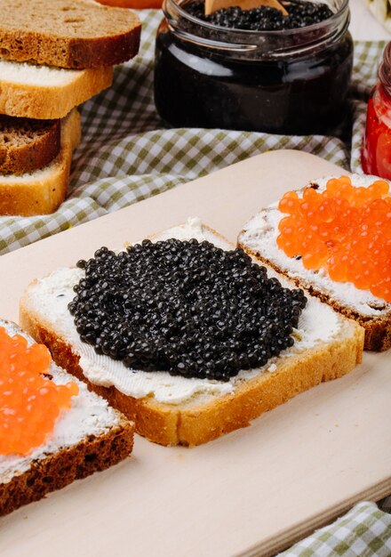 Vista lateral tostadas de caviar negro y rojo centeno y pan blanco con requesón caviar negro y caviar rojo sobre la mesa