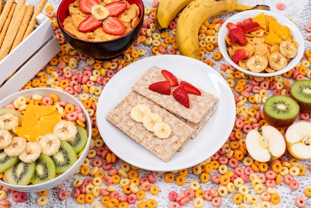 Vista lateral de tostadas con copos de maíz y frutas en superficie blanca horizontal