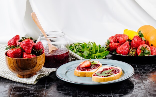 Vista lateral tostadas de fresa pan blanco con mermelada de fresa menta naranja y fresa fresca sobre la mesa