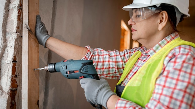 Foto gratuita vista lateral del trabajador de la construcción femenina con casco y taladro eléctrico